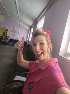 Woman in a pink outfit giving a thumbs-up in a room with a Prince's Trust logo.