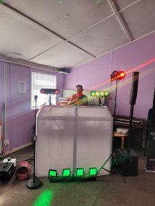 DJ setup with white enclosure, colorful lights, and sound equipment in a room.
