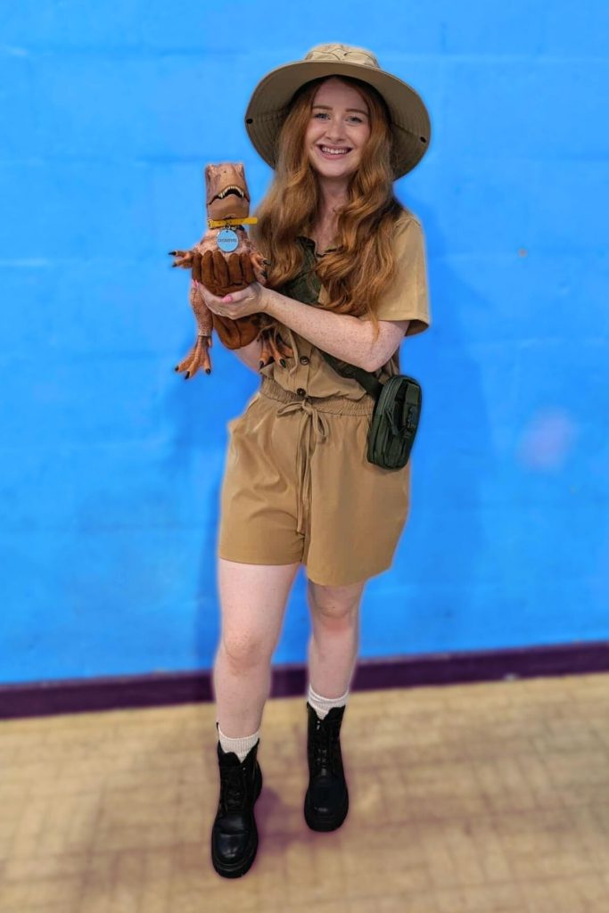 Woman in a dinosaur ranger costume with hat, holding a baby t rex