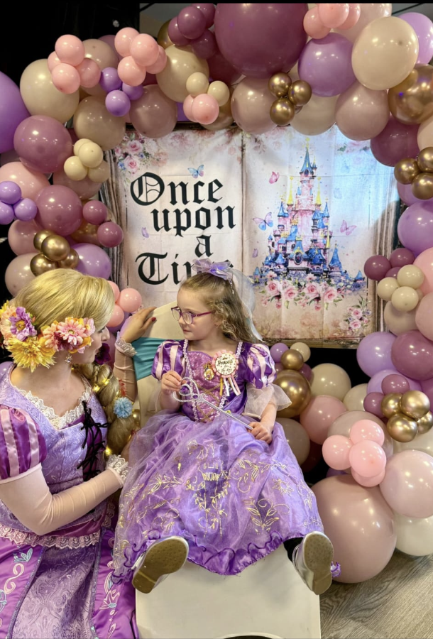 Princess entertainer dressed as Rapunzel posing with a child in a purple princess dress at a birthday party in Nottingham with pastel balloon backdrop and princess party setup by Absolutely Amazing Parties.