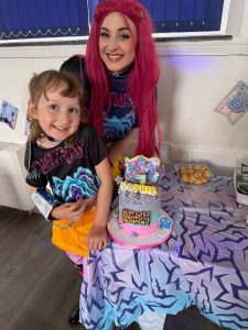 Entertainer dressed as Mira fro Demon Hunters with a small child also dressed as Mira by the side of a birthday cake