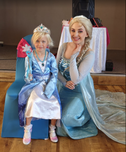 Actor dressed as Elsa sat wqith a child also dressed as Elsa